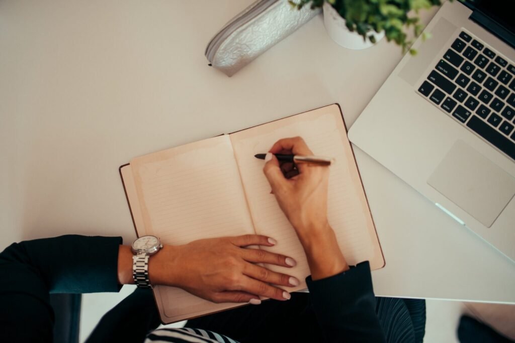A researcher writing notes in a notebook beside a laptop